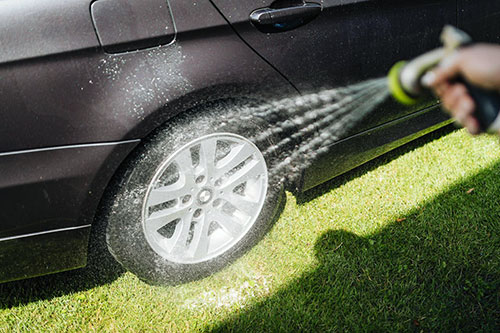 Someone using a house to wash a wheel rim on a black car